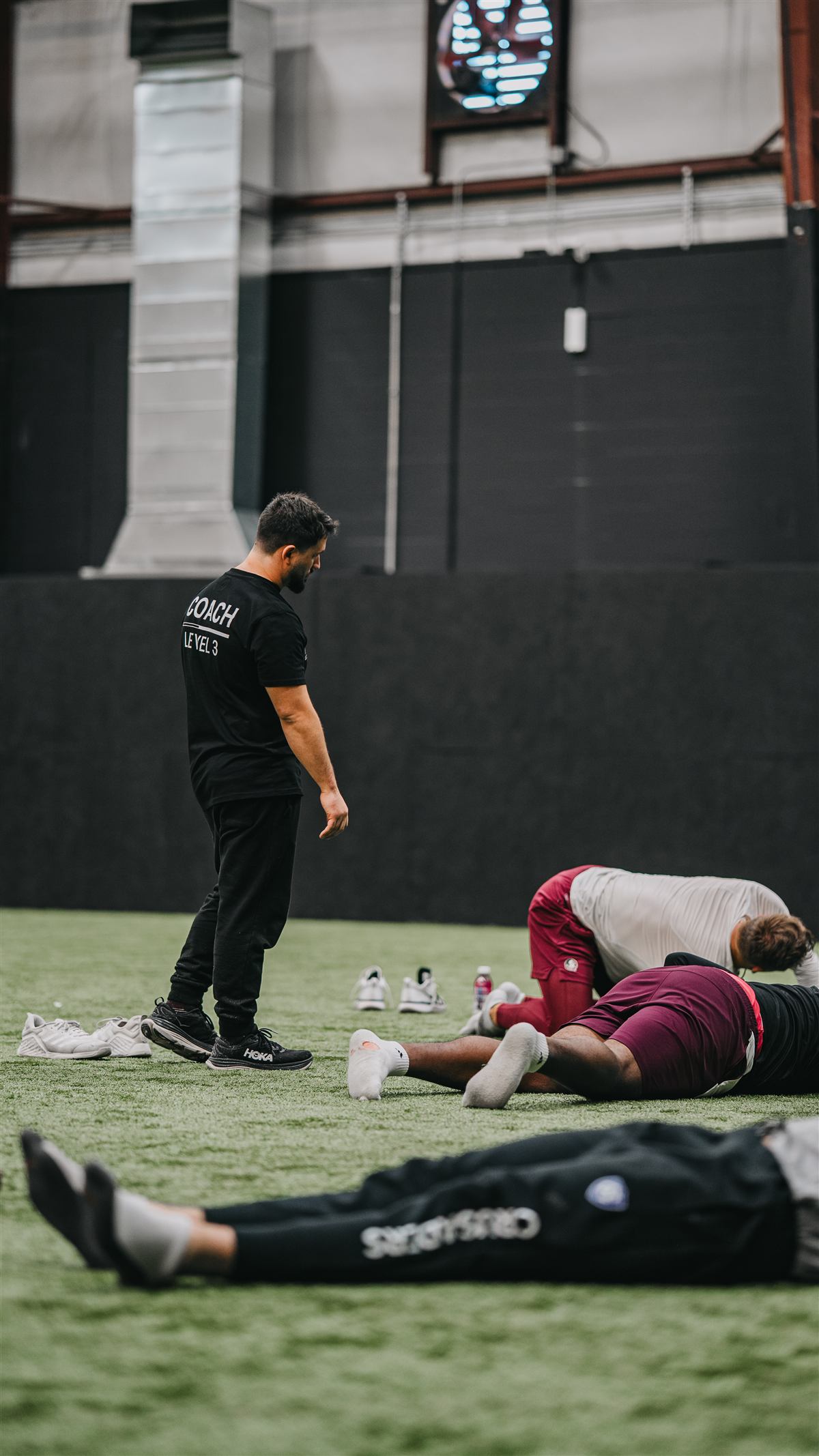 Coach Ellis Wells overseeing athletes doing mobility work on indoor turf