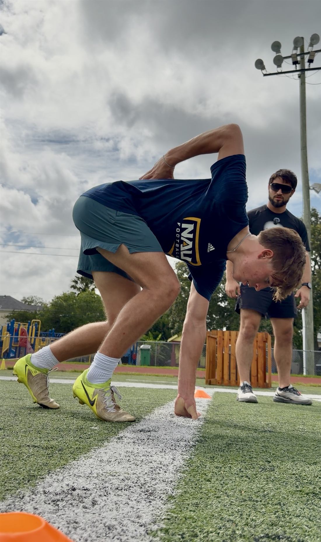A young athlete in a three-point sprint start stance while Coach Ellis Wells watches