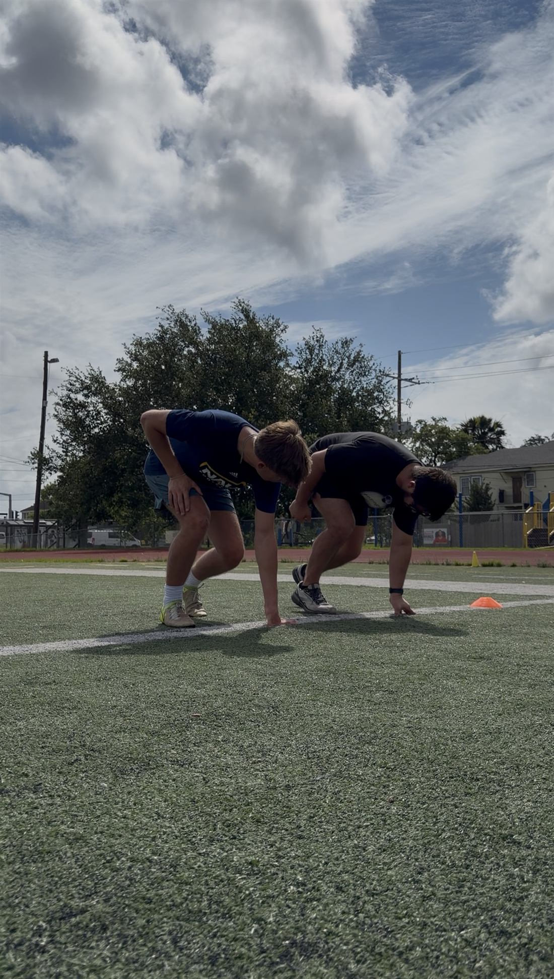 Ellis Wells demonstrating a three-point start stance side by side with a youth athlete